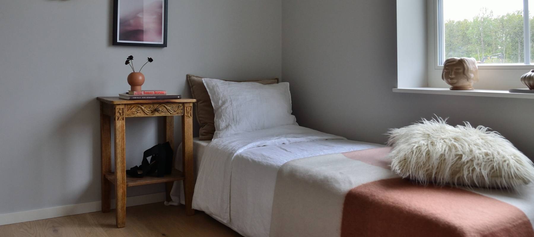 Single bed with sheet and wooden bedside table