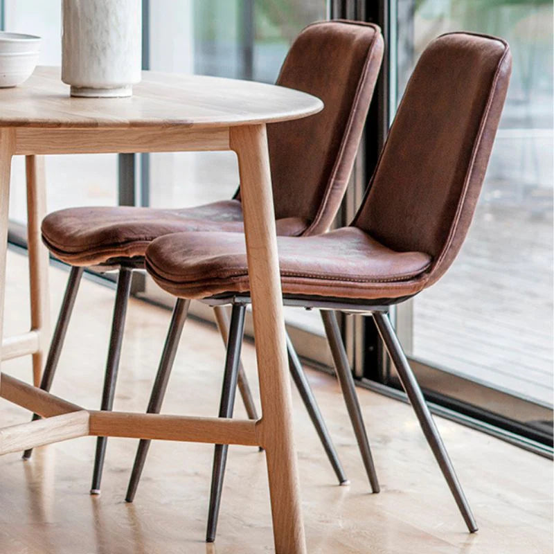 Trestle rustic dining table with two leather industrial dining chairs and sun shining across