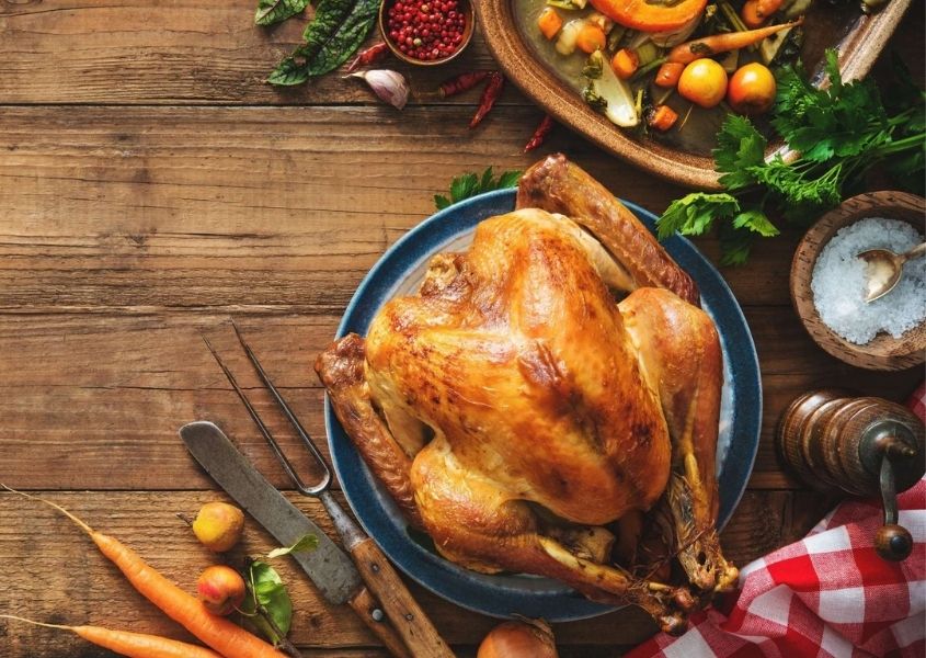 Close up of rustic table with whole roast turkey on plate and raw carrots and vegetables on table