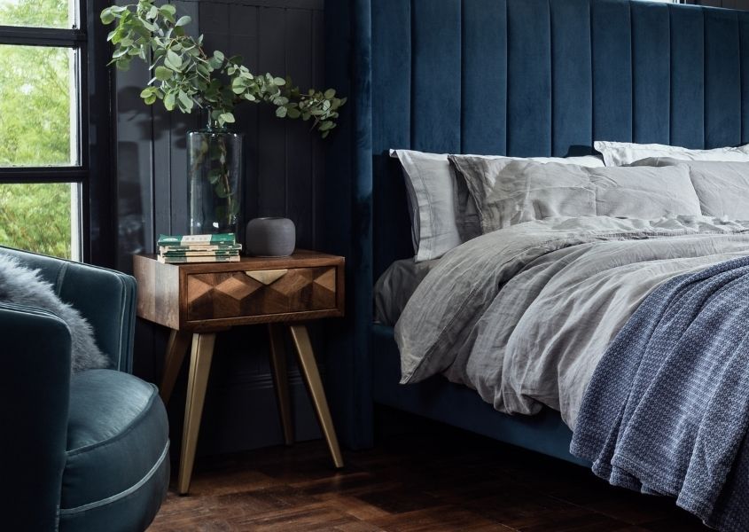mango wood bedside table next to dark blue velvet bed