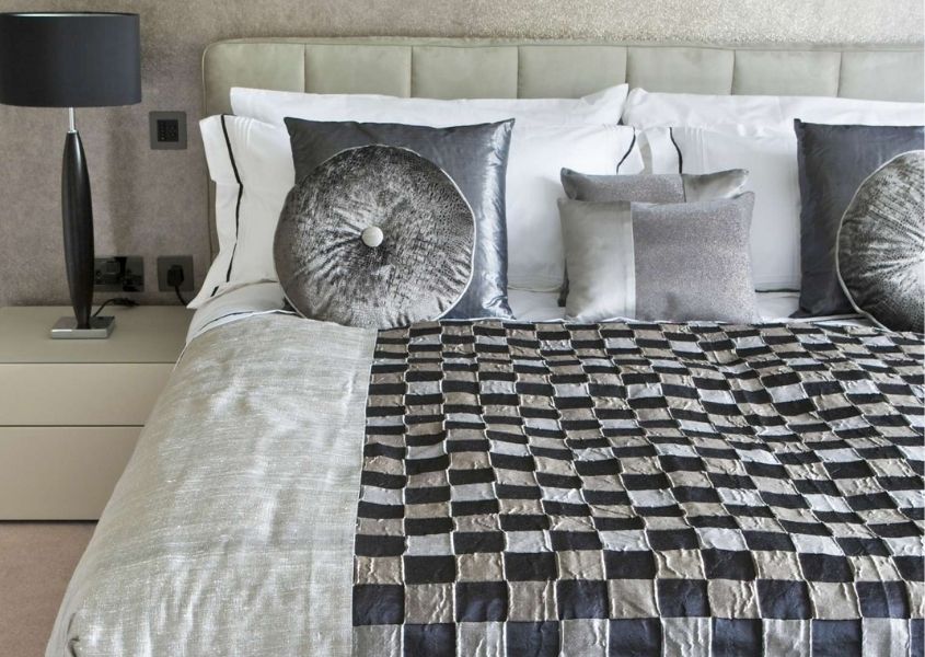Close up of silver bed covers and cushions with chequered bed throw