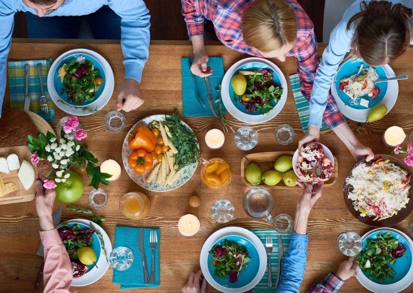 Group of people around a rustic dining table full of food and drinks raising their glasses